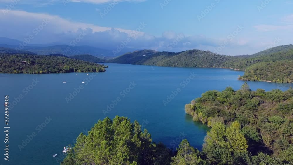 Aerial view of the lake surrounded by many green trees with mountains in the background Aerial view of the lake surrounded by many green trees with mountains in the background