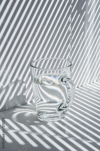 Still life with a glass mug and diagonal striped shadow (ID: 372701215)