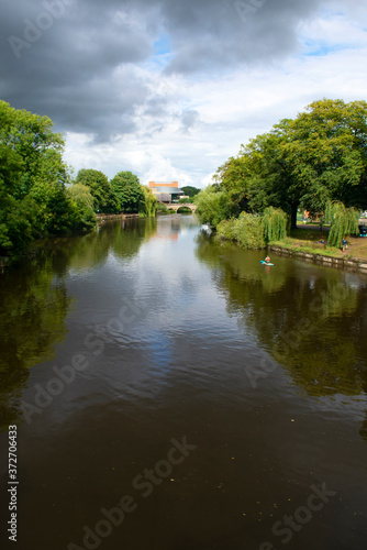 The river Severn flowing through the beautiful English town of Shrewsbury.  A summers scene with green parkland at the riverbank.  Trees are reflected on the calm river waters.  Copy space.