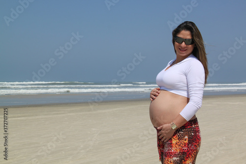 Mulher grávida na praia usando roupa branca. Retrato de uma futura mamãe. Barriga de uma mulher grávida.