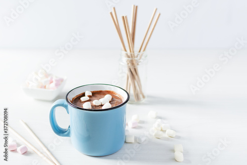Hot chocolate with marshmallows in a blue enamel mug on white table.