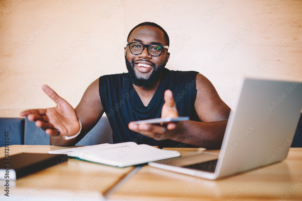 Cheerful african american guy gesturing and holding smartphone satisfied with prosperous freelance business, happy dark skinned male looking at camera smiling completed task of distance job Cheerful african american guy gesturing and holding smartphone satisfied with prosperous freelance business, happy dark skinned male looking at camera smiling completed task of distance job