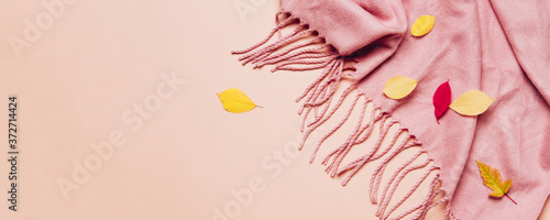Pink cozy scarf with tassels and scattered leaves on pastel banner photo