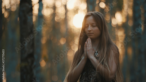 young woman praying with closed eyes in nature during the sunset surrounded by trees. High quality photo
