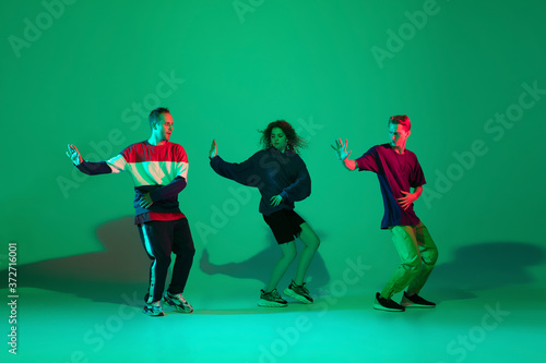 Action time. Stylish men and woman dancing hip-hop in bright clothes on green background at dance hall in neon light. Youth culture, movement, style and fashion, action. Fashionable portrait.
