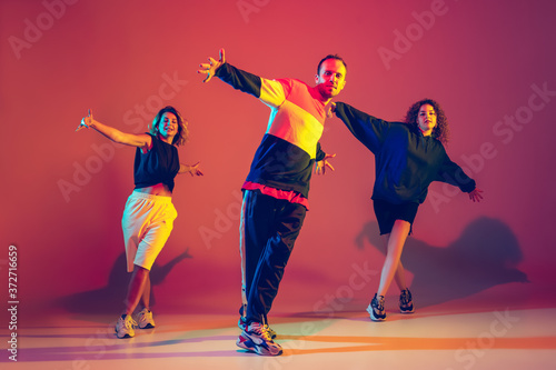 Dynamic. Stylish men and woman dancing hip-hop in bright clothes on green background at dance hall in neon light. Youth culture, movement, style and fashion, action. Fashionable portrait.