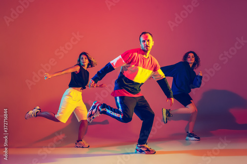 Dynamic. Stylish men and woman dancing hip-hop in bright clothes on green background at dance hall in neon light. Youth culture, movement, style and fashion, action. Fashionable portrait.