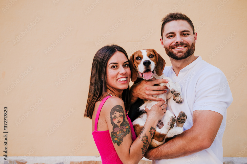 happy young couple outdoors kissing their beagle dog. Family and lifestyle concept. yellow background