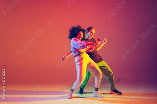 Drive in motion. Stylish man and woman dancing hip-hop in bright clothes on green background at dance hall in neon light. Youth culture, movement, style and fashion, action. Fashionable portrait.