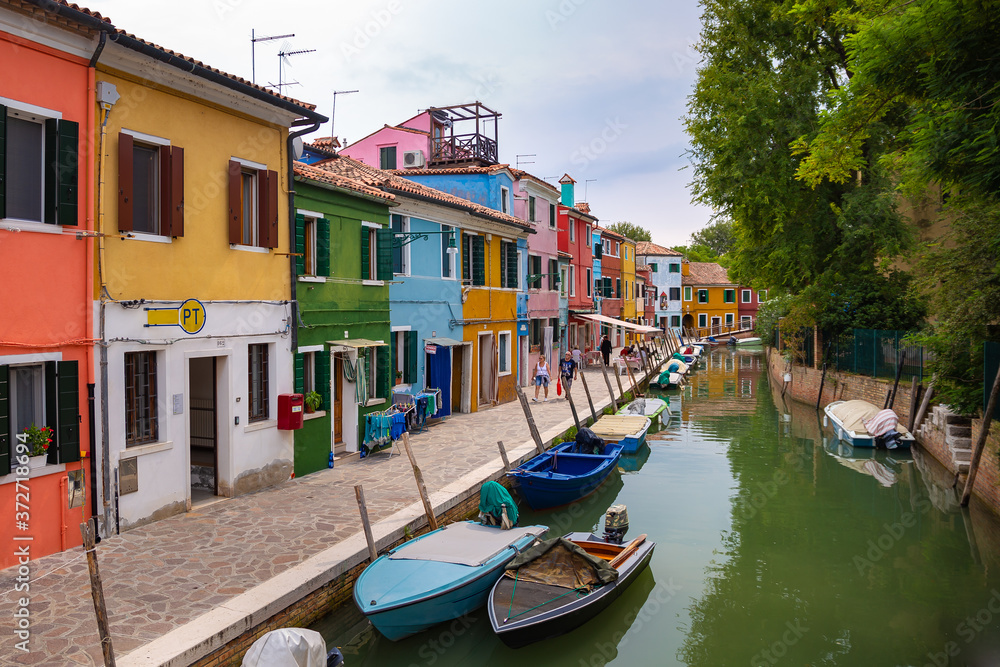 Burano, Italy - 09-18-2019 Colorful houses by canal in Burano, Italy. Burano is an island in the Venetian Lagoon and is known for its lace work and brightly colored homes.