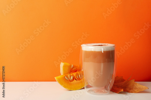 Glass of pumpkin latte, leaf and pumpkin on orange background