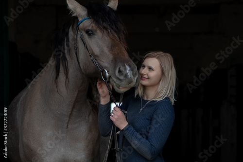 Portrait of a blonde girl with a horse on a dark background.