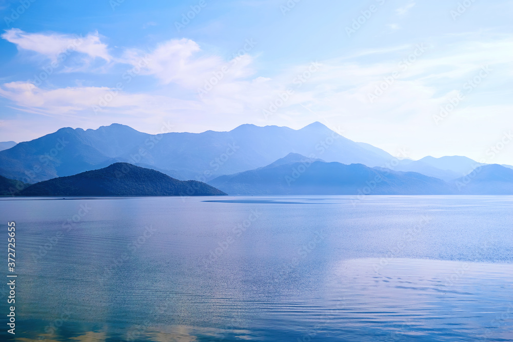 Twilight over the calm lake water and island with mountains. Famous Skadar lake in Montenegro. Nature background texture