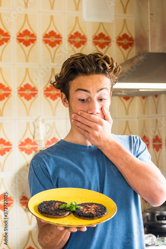 Surprised teenager after brned two hamburger cooked in the kitchen at home - young boy do chef and mistakes.- funny people real life scene photo