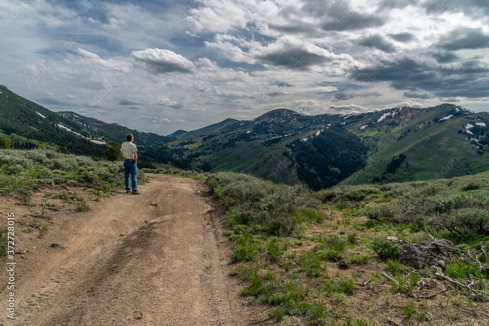 A man standing on a dirt road, path, watching a scene of distance mountains and dramatic clouds in the sky, Bear Creek Summit, Jarbidge, Nevada