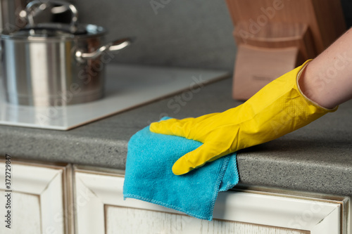 Woman's hands in yellow gloves cleaning counter top in kitchen