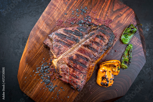 Traditionelles gegrilltes dry aged Wagyu Porterhouse Steak vom Rind angeboten mit Paprika und Chili als Draufsicht auf einem Modern Design Holz Board