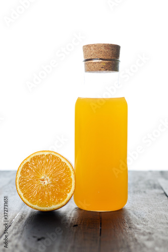 a glass bottle of fresh and cool orange juice with fresh half orange fruit on a table isolated on a white background