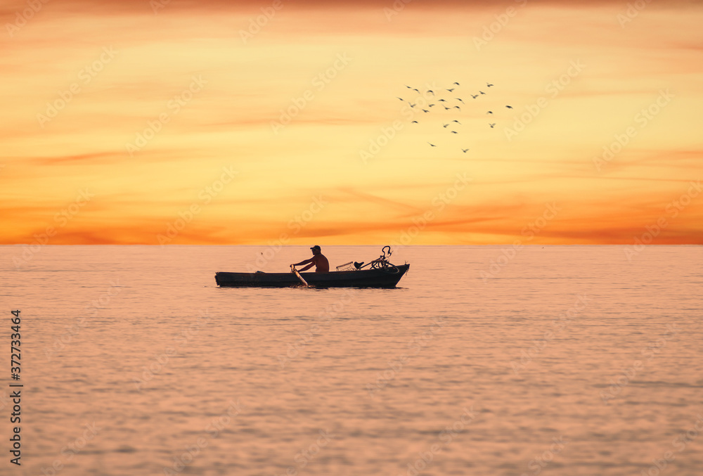 Boat on the water. There is a man and a bicycle in the boat. Silhouettes at sunset. Birds in flight