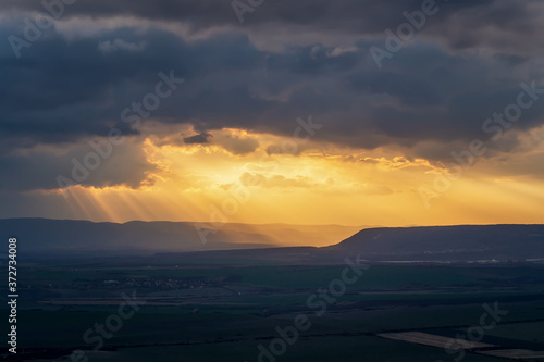 Amazing long shot of sunlight and sun beams in sky at sunset over green field © Jess_Ivanova