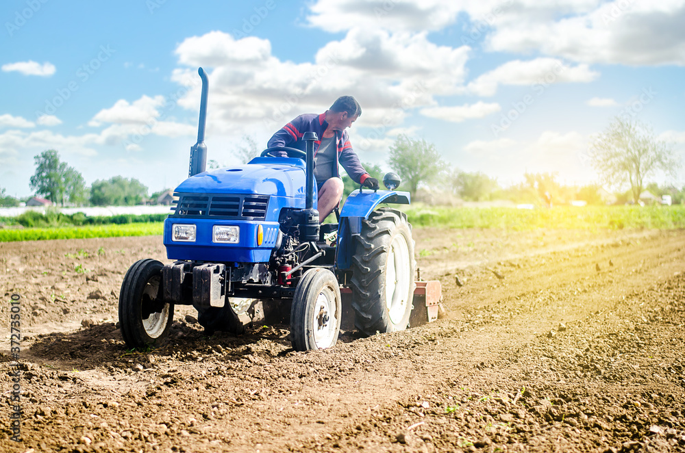 Fototapeta Farmer on a tractor loosens the soil with milling equipment. Loosening surface, land cultivation Use of agricultural machinery and to simplify and speed up work. Farming, agriculture. Plowing field.