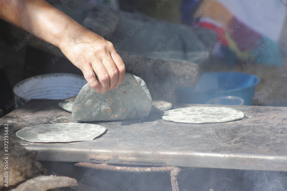 Hands of indigenous women making blue corn tortillas in a traditional way in rustic kitchen