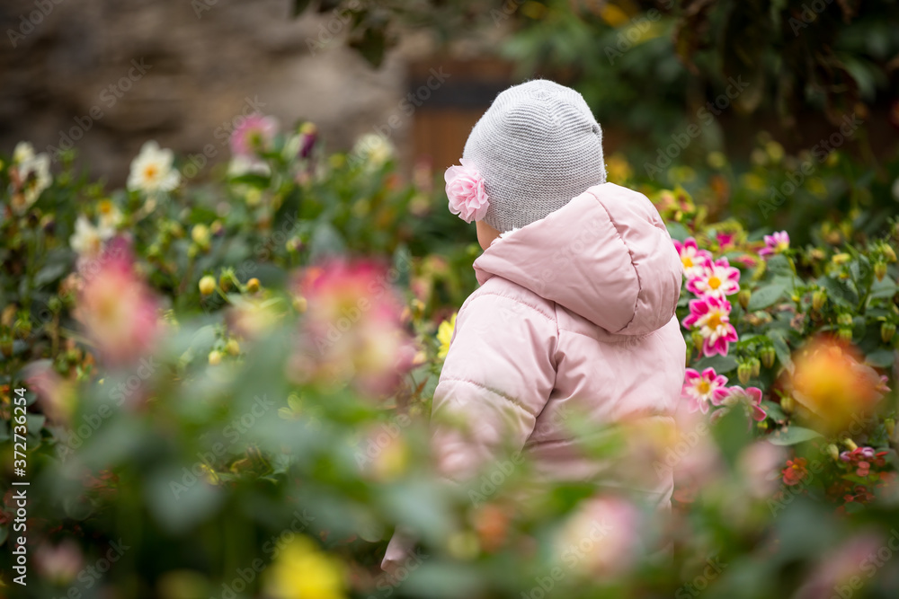 A little child (girl) in a garden surrounded by roses and other flowers in Cesky Krumlov, Czechia