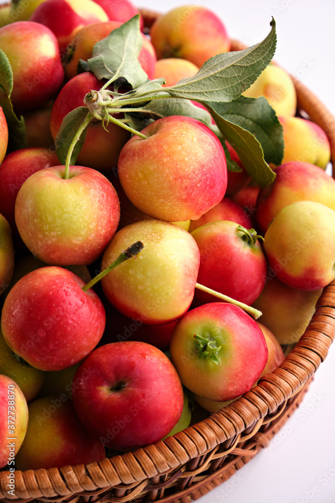 Red and yellow ripe apples with leaves close-up in a wicker basket on a light background. Close up. No people Red and yellow ripe apples with leaves close-up in a wicker basket on a light background. Close up. No people