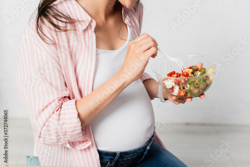 partial view of pregnant woman holding plastic fork near takeaway container with fresh salad