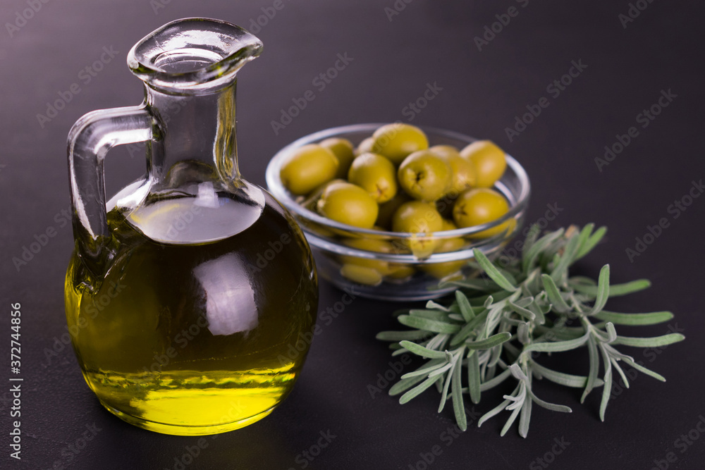 Olive oil in a decanter and a sprig of rosemary on a black background. Olive oil in a decanter and a sprig of rosemary on a black background.