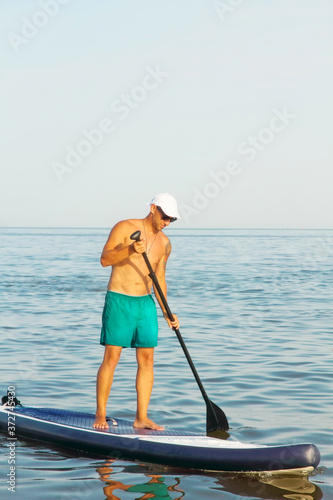 Man is training on a SUP board in the summer sea.