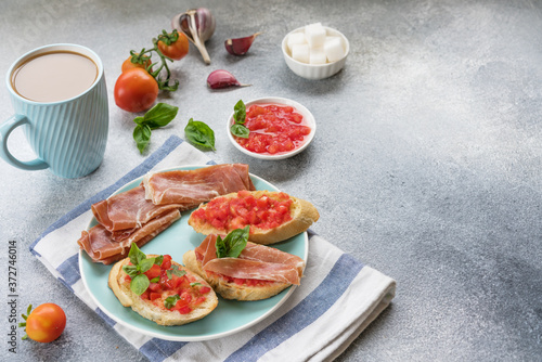bruschetta, toast with sliced tomatoes, jamon and Basil on a blue plate, and coffee with milk in a blue Cup. copy space