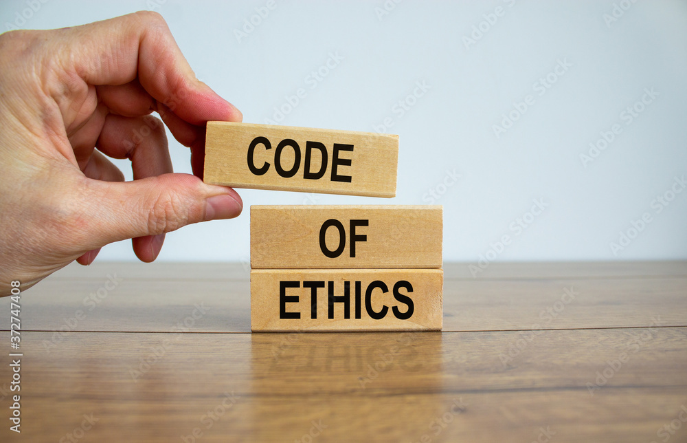 Male hand placing a blocks with word 'code' on top of a blocks tower. Text 'code of ethics'. Beautiful white background. Copy space. Male hand placing a blocks with word 'code' on top of a blocks tower. Text 'code of ethics'. Beautiful white background. Copy space.