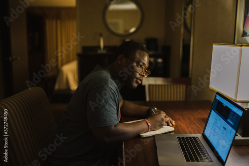 Young man taking notes while watching laptop presentation at home