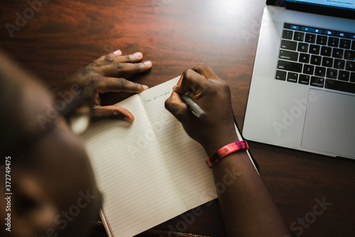 Overhead view of man writing in notebook next to laptop