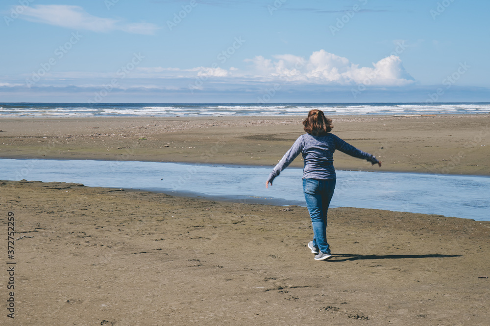 Woman Walking Alone Along an Ocean Beach with Wind Blowing Her Hair 