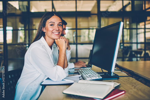 Happy female employee resting during work break looking at camera enjoying time in office, portrait of brunette cheerful woman satisfied with occupation collaborating with male colleague for project