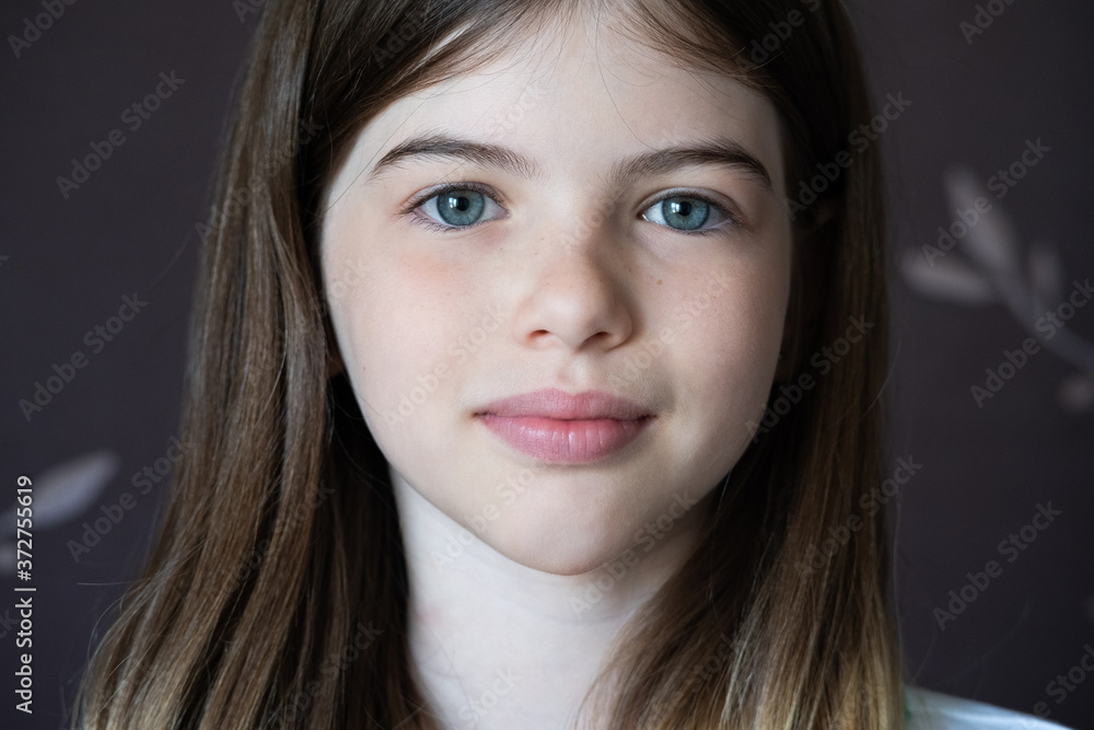 The face of a young beautiful girl, a child close up. Portrait of a brunette girl with long hair and blue eyes on a dark background The face of a young beautiful girl, a child close up. Portrait of a brunette girl with long hair and blue eyes on a dark background