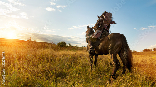 Girl in medieval knight s armor is riding a horse against the sunset fields background