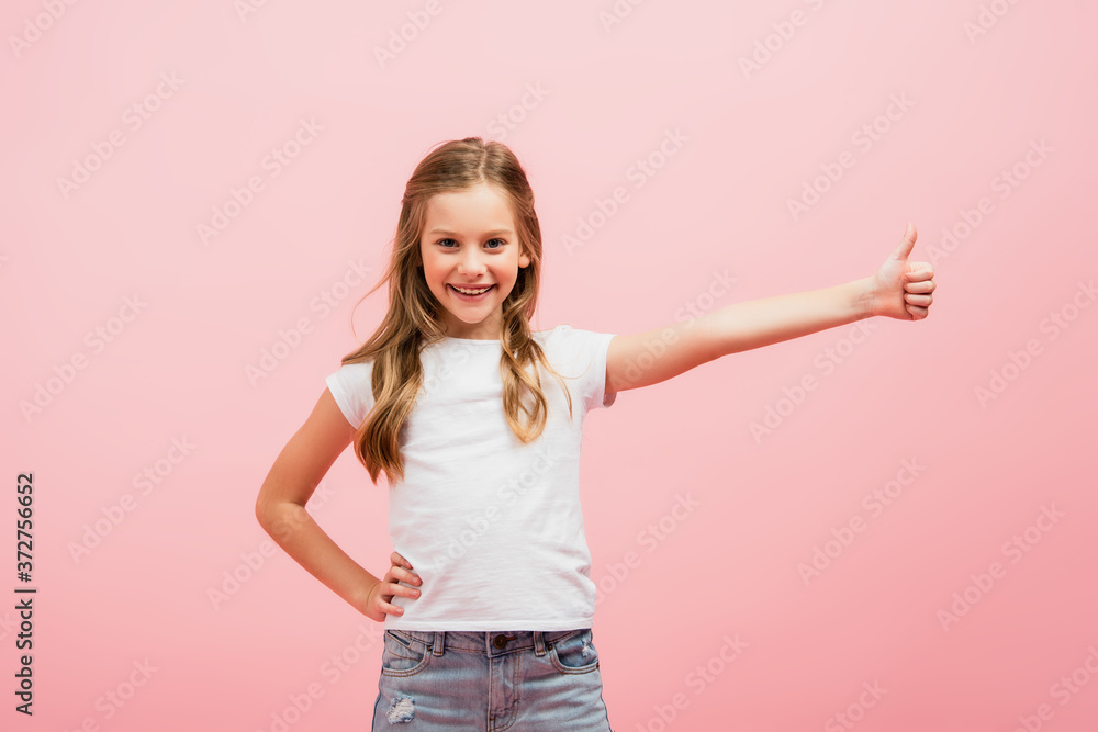 child in white t-shirt with hand on hip showing thumb up while looking at camera isolated on pink child in white t-shirt with hand on hip showing thumb up while looking at camera isolated on pink