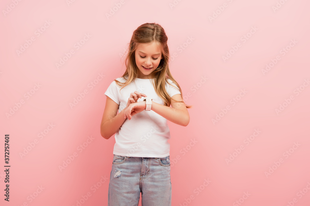 child in white t-shirt and jeans touching smartwatch isolated on pink child in white t-shirt and jeans touching smartwatch isolated on pink