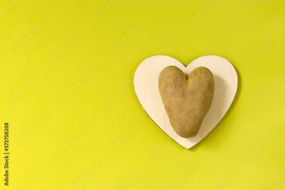 Obraz premium Ugly potatoes in the shape of a heart on a wooden board on a green background. Unusual concept of vegetables. horizontal orientation. Top view. Copy space.