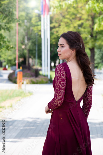 girl's back in a beautiful long burgundy dress in the summer on a city street