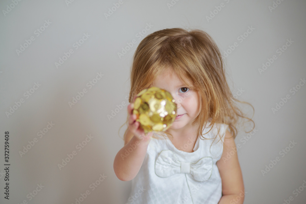 Redhair girl with gold christmas ornament on light gray background Redhair girl with gold christmas ornament on light gray background