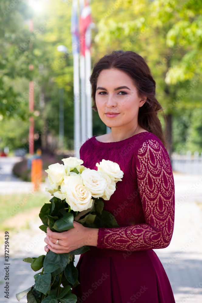 Fototapeta premium girl in a beautiful long burgundy dress with a white bouquet of roses
