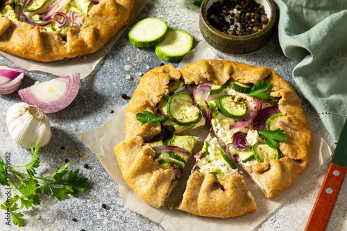 Healthy pastries made from rye flour, dessert diet food. Galette with zucchini, onions and feta on a light stone table.