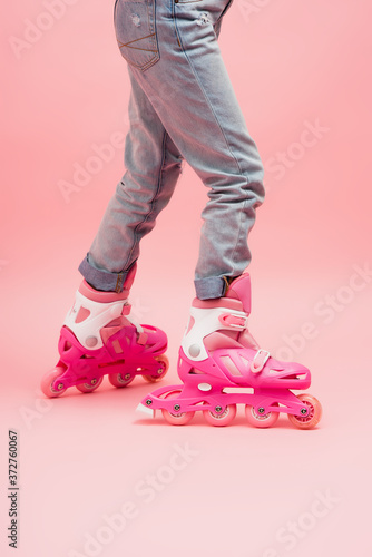 cropped view of child in jeans and rolling skates on pink