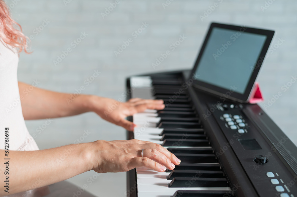 Fototapeta premium A woman watches video lessons on a digital tablet and plays on an electro synthesizer. The girl learns to play the piano remotely.
