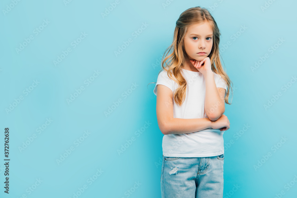 upset girl in white t-shirt looking at camera while holding hand near face isolated on blue upset girl in white t-shirt looking at camera while holding hand near face isolated on blue