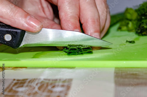 A housewife is slicing green onions on a chopping Board.